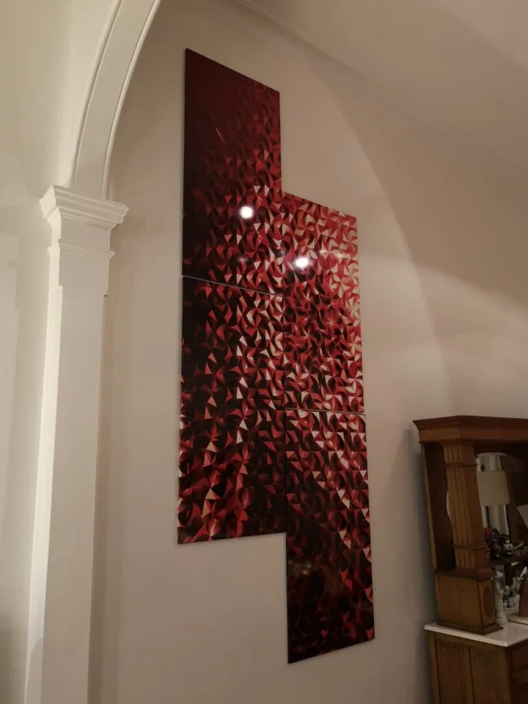 Cuatro cuadros sin marco dispuestos en forma de pared de ladrillos, representando una única imagen de geometría 3D tipo bajo relieve, predominando el color rojo, impresos en vinilo y laqueados brillantes, obra de Javier Colomino